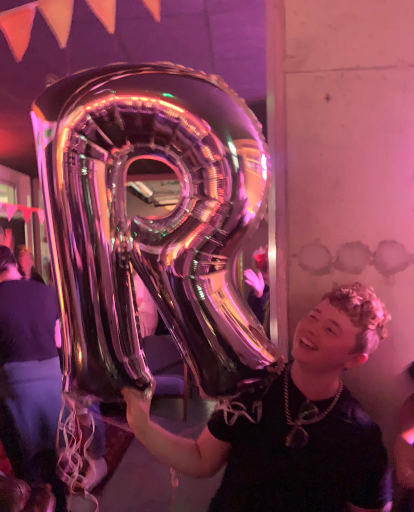 Ruadhán Ó Críodáin with a giant "R" balloon in a bar.