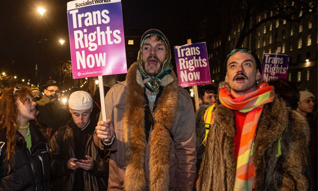 Protestors hold up signs reading 'trans rights now.'