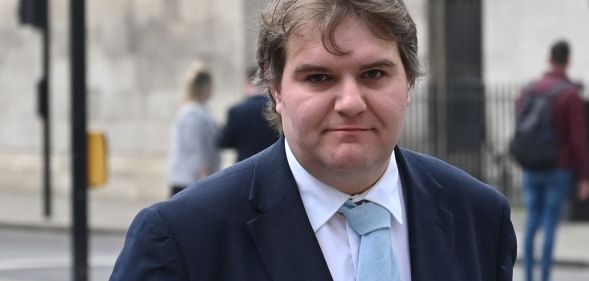 Jamie Wallis wears a white shirt, light blue tie and dark blue jacket while standing outside