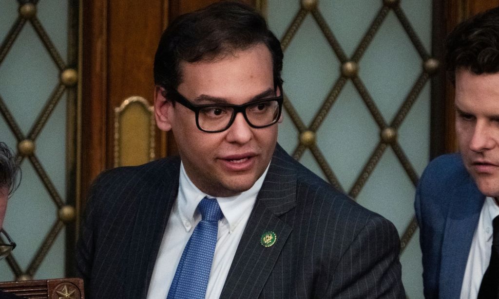 George Santos wears a suit and tie while standing next to other politicians in the US House of Representatives