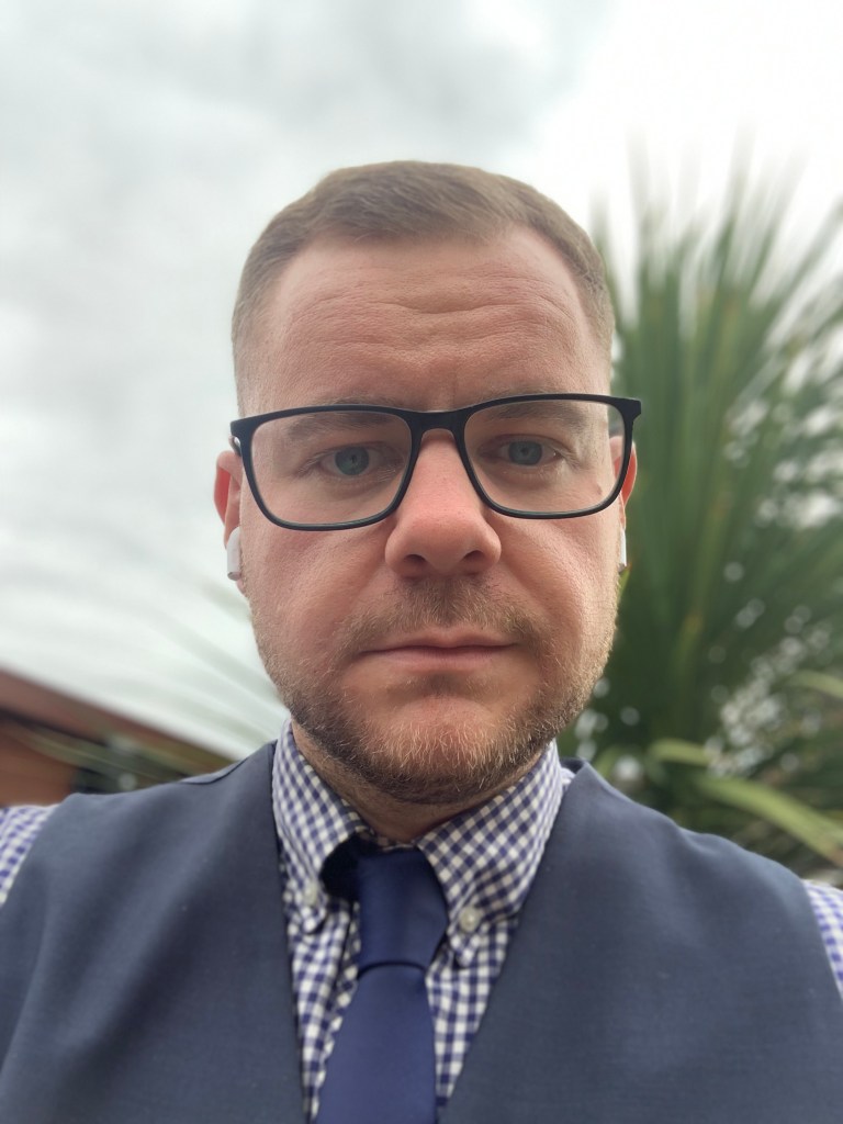 Steven Grocock, a gay man, is pictured outdoors wearing a waistcoat, shirt and tie. He is wearing glasses and has brown hair. 