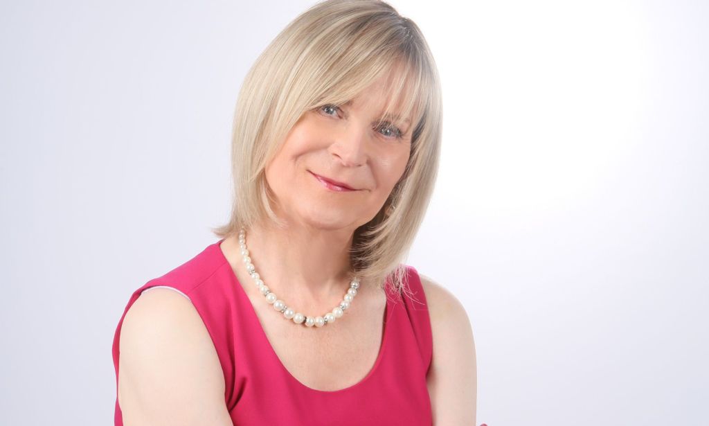 Steph Richards, founder of TransLucent, smiles at the camera while wearing a red outfit and white necklace