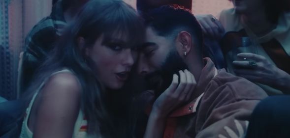 Taylor Swift looks towards the camera as she holds the face of Laith Ashley, a trans model and singer, in a house party scene in her "Lavender Haze" music video