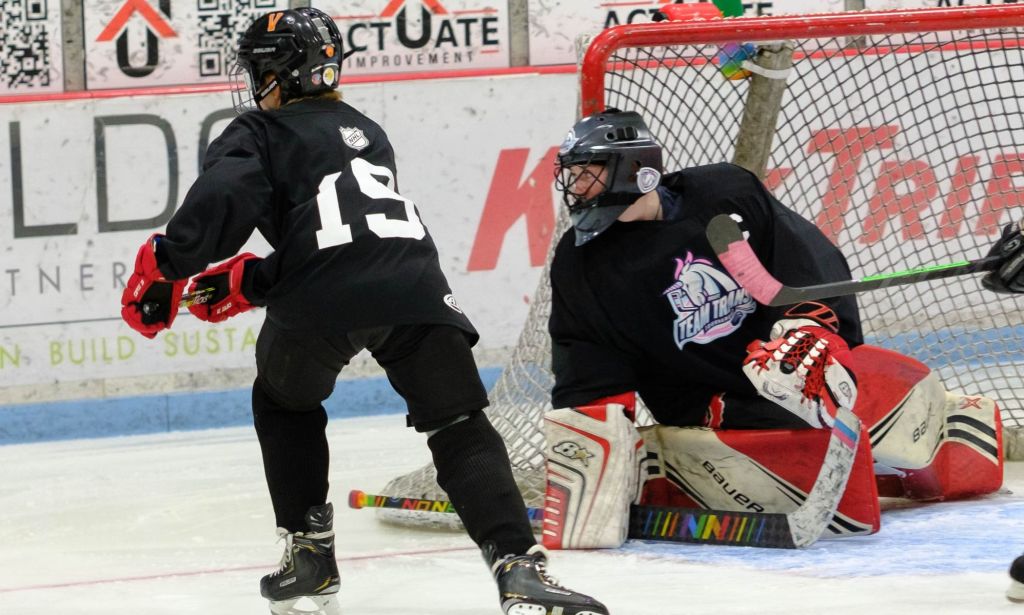 A Team Trans hockey player approaches the goal on skates while the goalie is posed on the ice in front of the goal