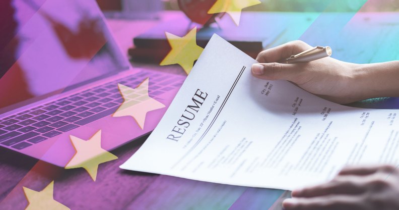 A pair of hands are holding a CV on a desk with a computer in the background.