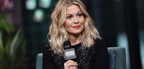 Candace Cameron Bure smiling, wearing a black top and holding a microphone.