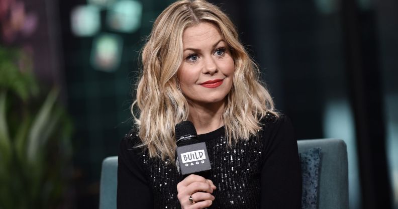 Candace Cameron Bure smiling, wearing a black top and holding a microphone.