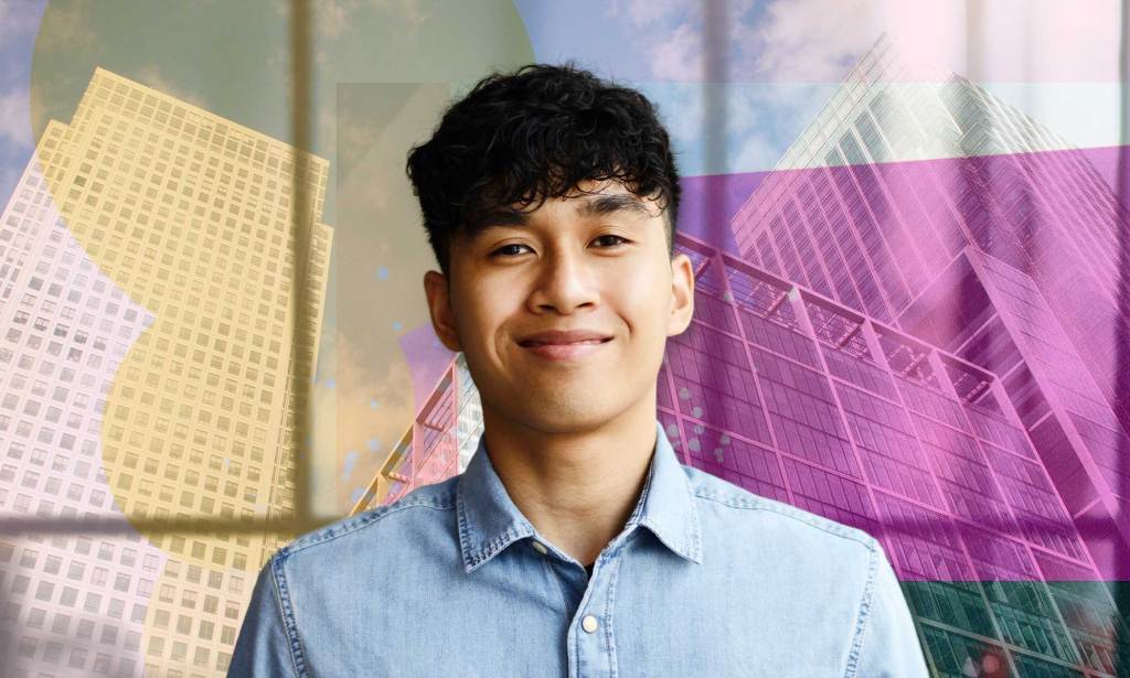 A masculine presenting person in a blue shirt smiles as they look into the camera.