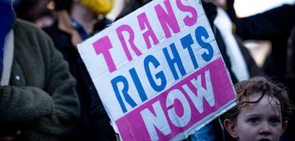 Pro-trans activists hold up a 'Trans Rights Now' placard.