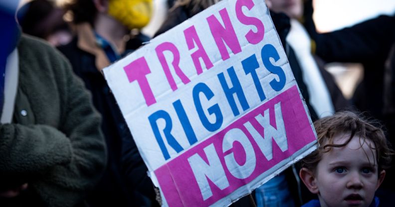 Pro-trans activists hold up a 'Trans Rights Now' placard.