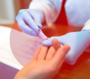 A medical professional's gloved hands as they take a blood sample from a person's finger to test for HIV.