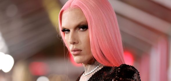 Jeffree Star looks at the camera wearing a pink straight wig, dark top and white necklace.