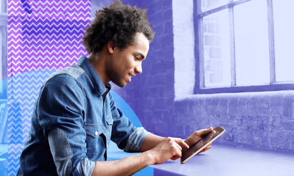 A man in a blue shirt is looking at his tablet.