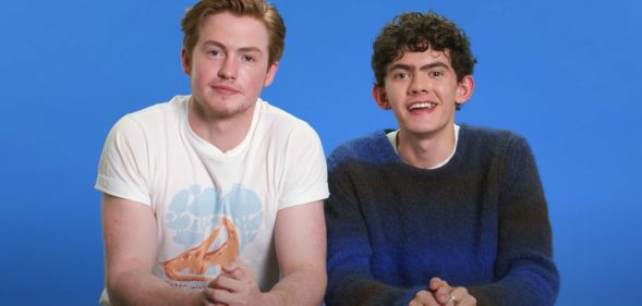 Kit Connor and Joe Locke sit next to each other against a blue background.