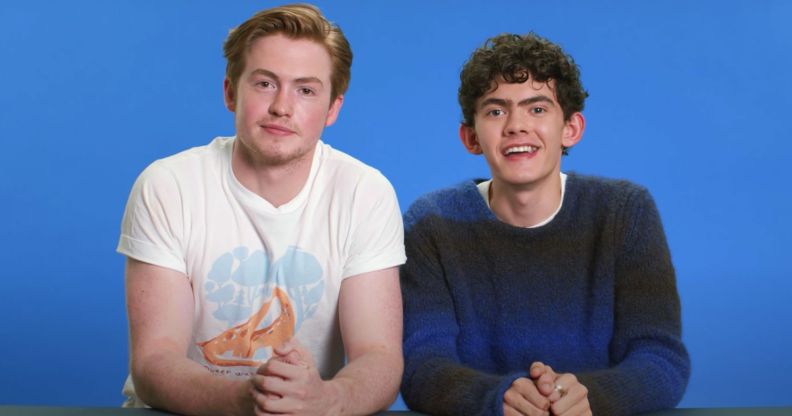 Kit Connor and Joe Locke sit next to each other against a blue background.