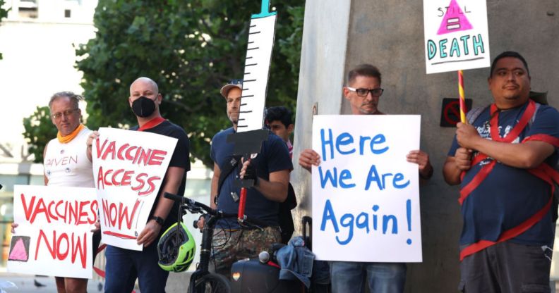 The LGBTQ+ community comes together for a protest about monkeypox. People hold signs that say "here we are again" and imploring the government to get more vaccines.