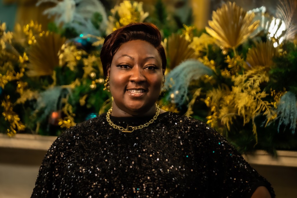 Lady Phyll is weraing a sparkly necklace and jumper and smiling for the camera.