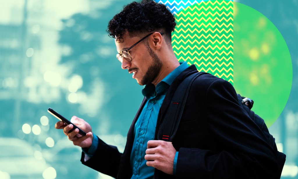 A man is carrying his backpack while looking down at his phone.