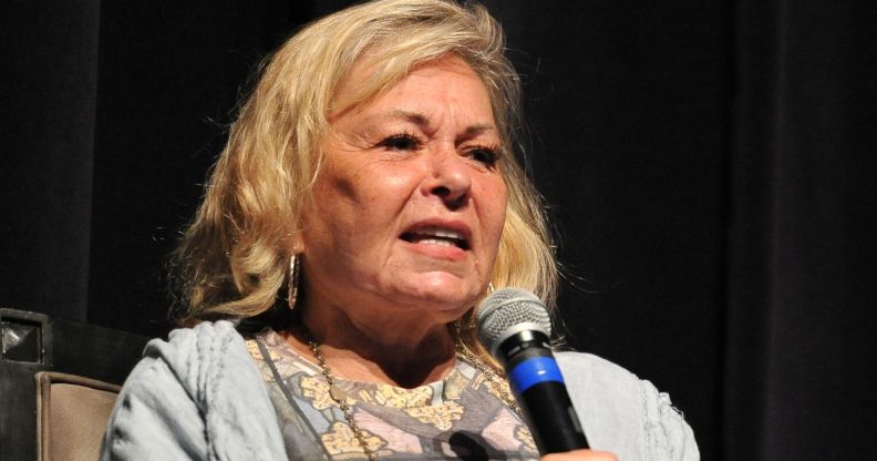 Roseanne barr wearing a patterned top and grey cardigan holding a black and blue microphone.