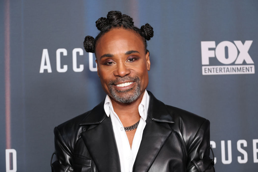 Billy Porter with his hair in bantu knots, wearing a white shirt and leather jacket