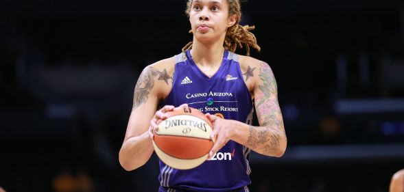 Brittney Griner wears a purple Phoenix Mercury basketball uniform as she holds a white and orange basketball in her hands