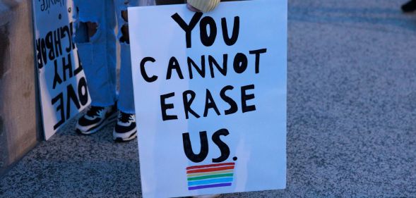 A person holds a sign reading 'You cannot erase us' with a rainbow LGBTQ+ flag below it during a protest against Republish's pushing 'Don't Say Gay or Trans' bills