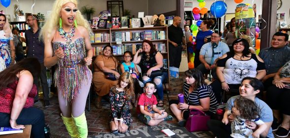 A drag queen wearing a sparking outfit dances while performing before a young audience at a reading event