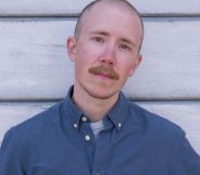 Trans activist and journalist Freddy McConnell wears a blue shirt as he stands in front of panelling