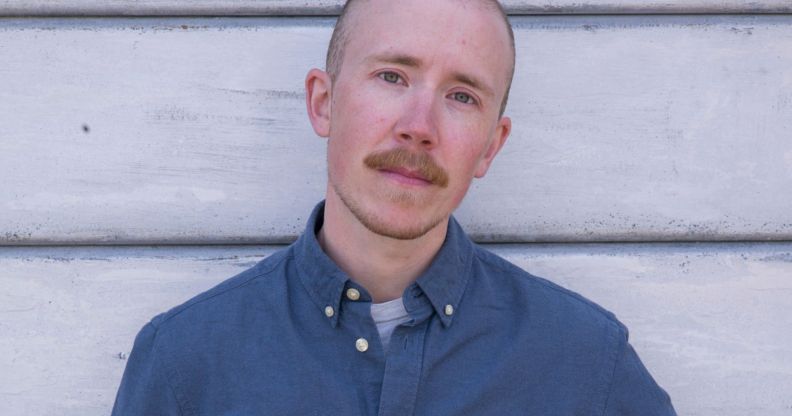 Trans activist and journalist Freddy McConnell wears a blue shirt as he stands in front of panelling