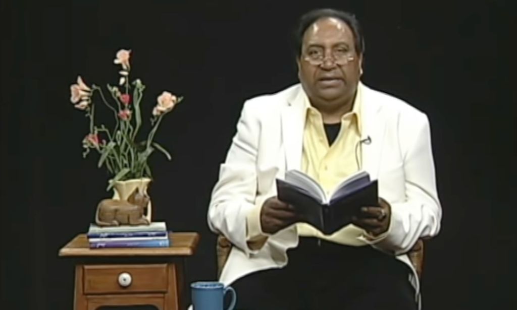 Gay Pakistani poet Ifti Nasim wears a white outfit with dark trousers as he reads aloud from a book of his poetry