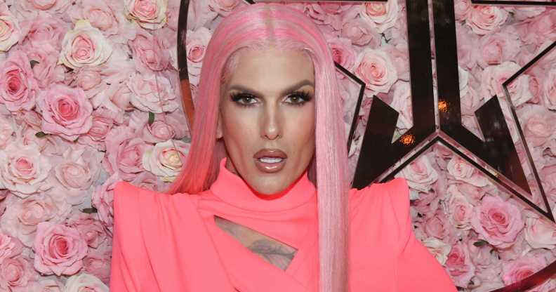 Photo of makeup artist Jeffree Star wearing a pink dress and pink wig standing in front of a background of pink roses