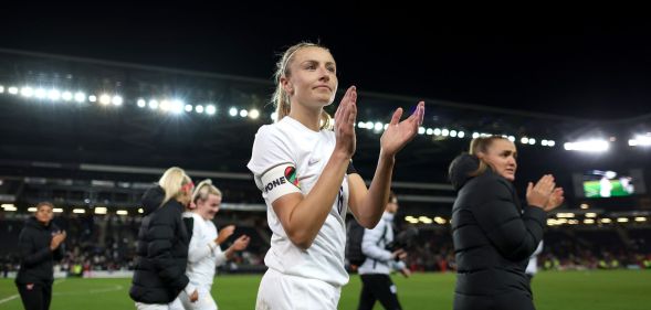 Lionesses captain Leah Williamson claps as she walks off the football field while wearing a white uniform and the rainbow OneLove armband