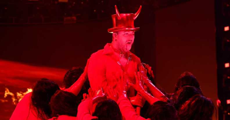 A screenshot from the 2023 Grammys ceremony shows Sam Smith performing "Unholy" on stage wearing a hat showing devil horns as a red spotlight casts a strong red light over him