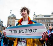 A person is holding a skateboard with the colors of the transgender flag and with a message in support of trans people.