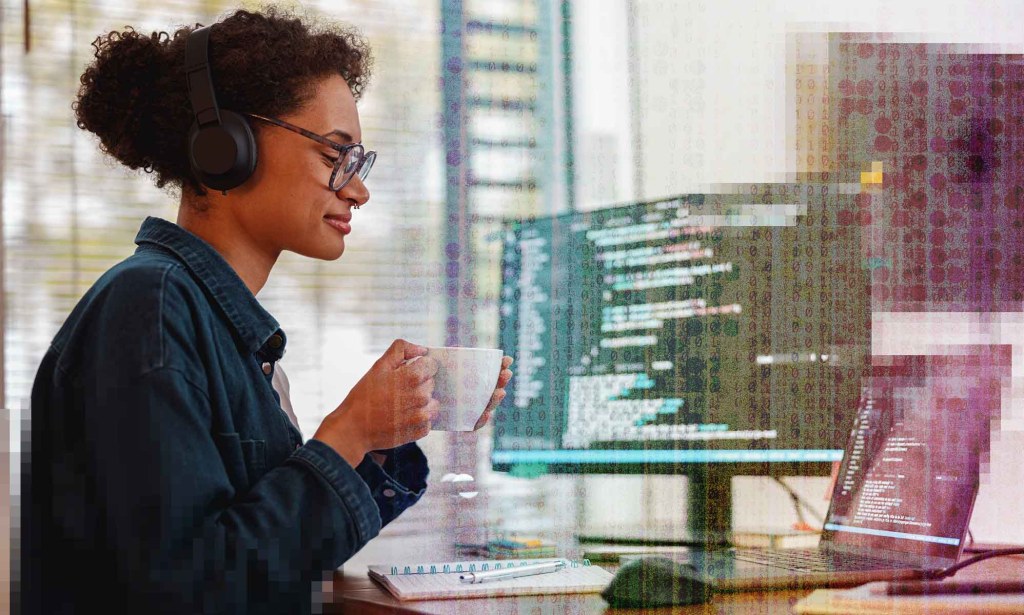 A woman is drinking a cup of coffee in front of a computer monitor displaying lines of code.