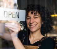 A woman with curly hair is turning over an "open" sign behind a glass door.