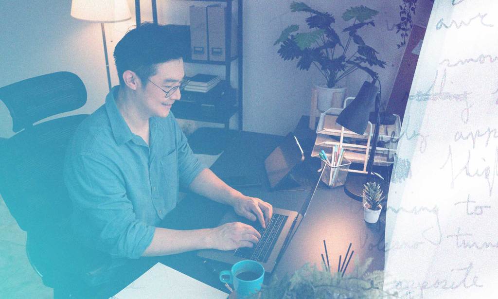 A person is at their computer in their home office smiling at the screen with a cup of coffee or tea.