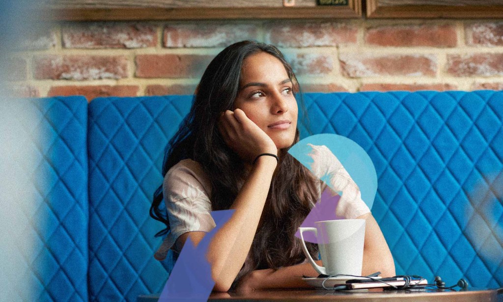 A woman is sitting with her head on her hand in a coffee shop.