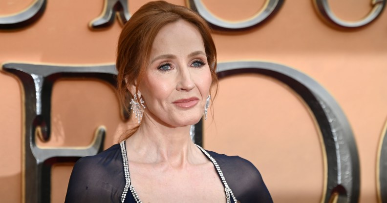 JK Rowling wears a navy blue dress against an orange background at a film premiere