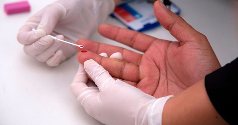 An image shows a person having a HIV test with a blood prick on their finger.