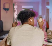 A young person has his back to the camera. He has an Apple Airpod in one ear and in each hand he is using a stimulant toy.