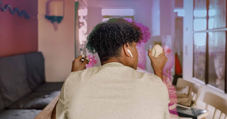 A young person has his back to the camera. He has an Apple Airpod in one ear and in each hand he is using a stimulant toy.