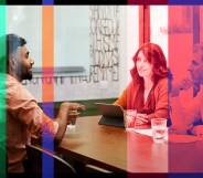 A man in a beard is sitting across from a man and woman in a conference room setting in an office.