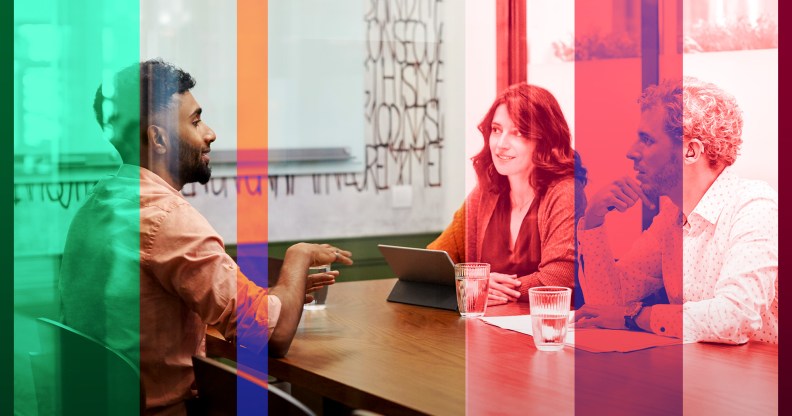 A man in a beard is sitting across from a man and woman in a conference room setting in an office.