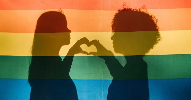 People making a heart shape behind a pride flag