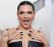 Mae Muller wears a black dress at the MTV 2022 VMAs, looking off camera, hands on her shoulders, and with her mouth open.