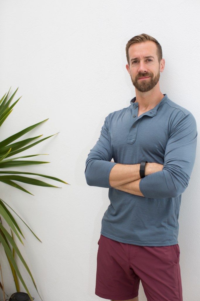 Matt Boyles pictured indoors wearing exercise clothing while standing beside a plant.