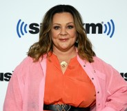 Cropped head and chest image of Melissa McCarthy who has spoken up against Tennessee Drag ban. She is wearing a orange top with a pink cardigan on a white background with Sirius XM logo.