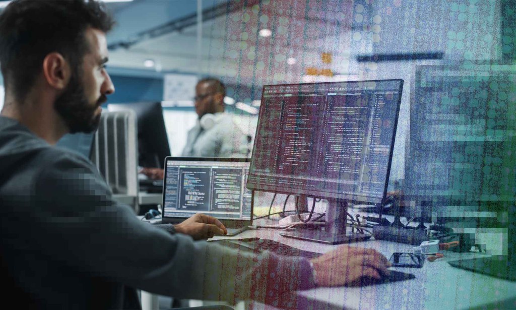 A bearded man sits in front of a dual-monitor display.