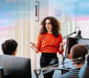 A person speaking in an office with trans Pride flag colours superimposed behind